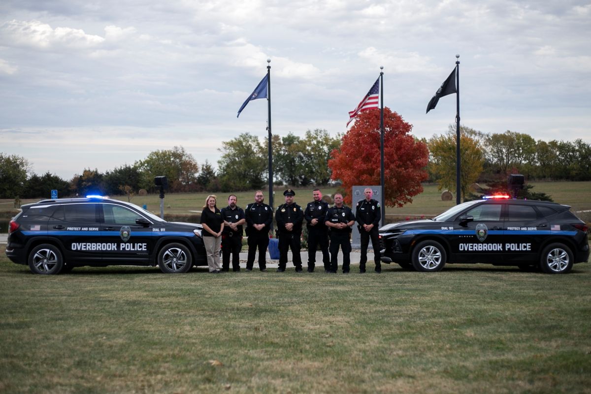 Photo of police department standing in between police cars in front of flags