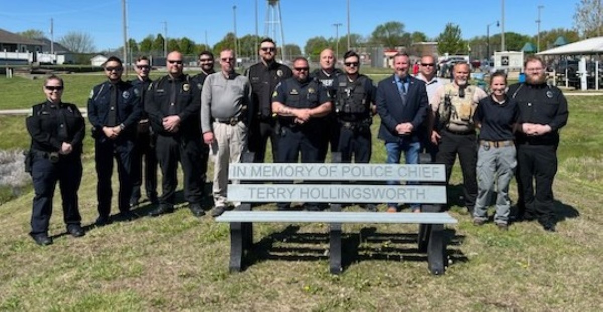 Photo of officers gathered around bench dedicated to late Police Chief Terry Hollingsworth